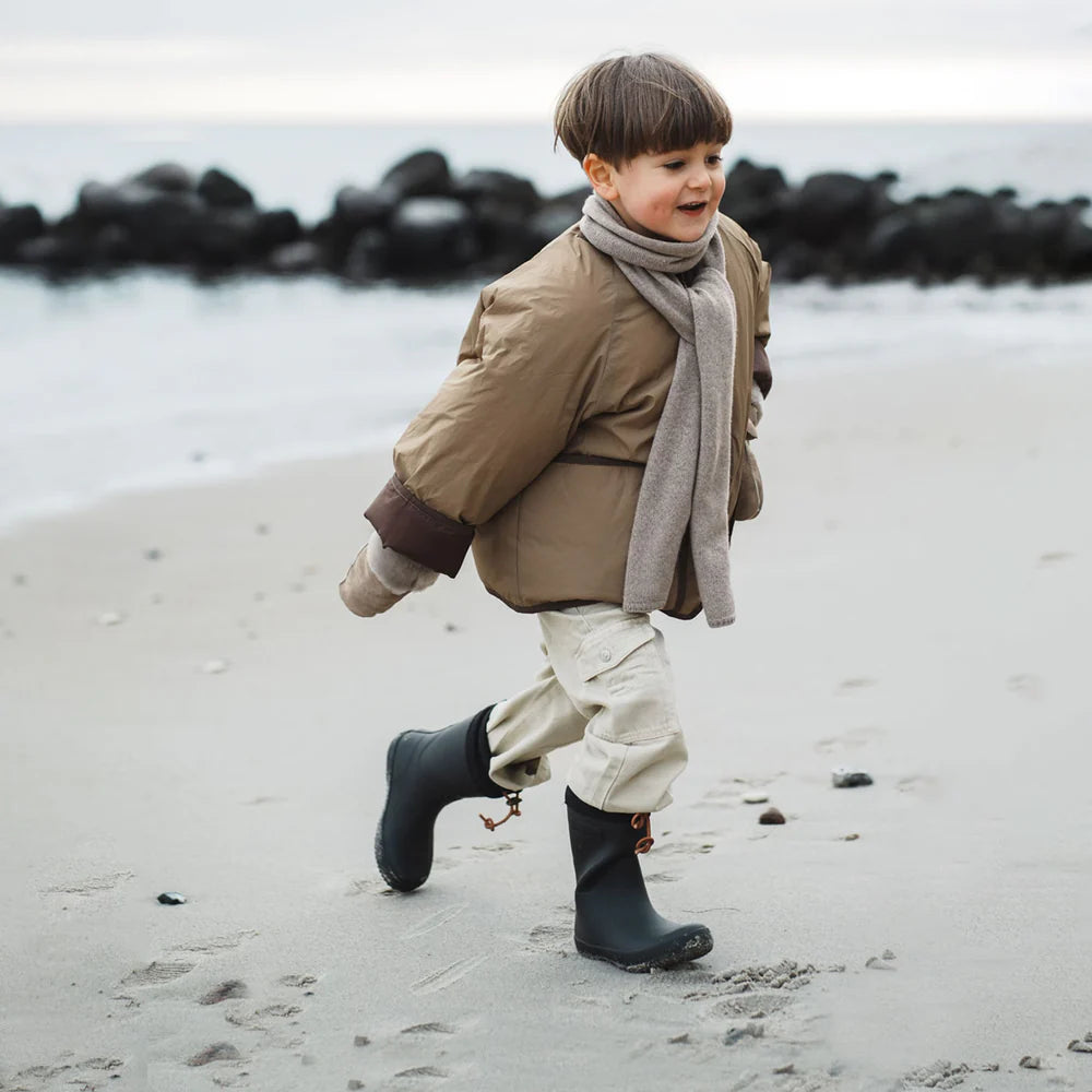 Child in a beige coat and black boots running on a beach.
